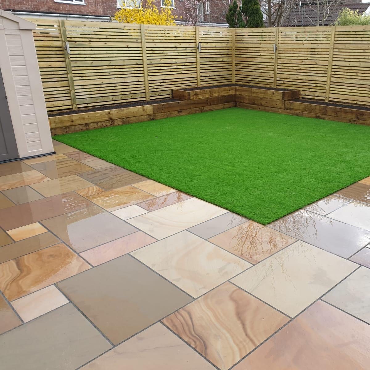 Patio with natural stone tiles and artificial grass, showcasing a clean and polished finish.