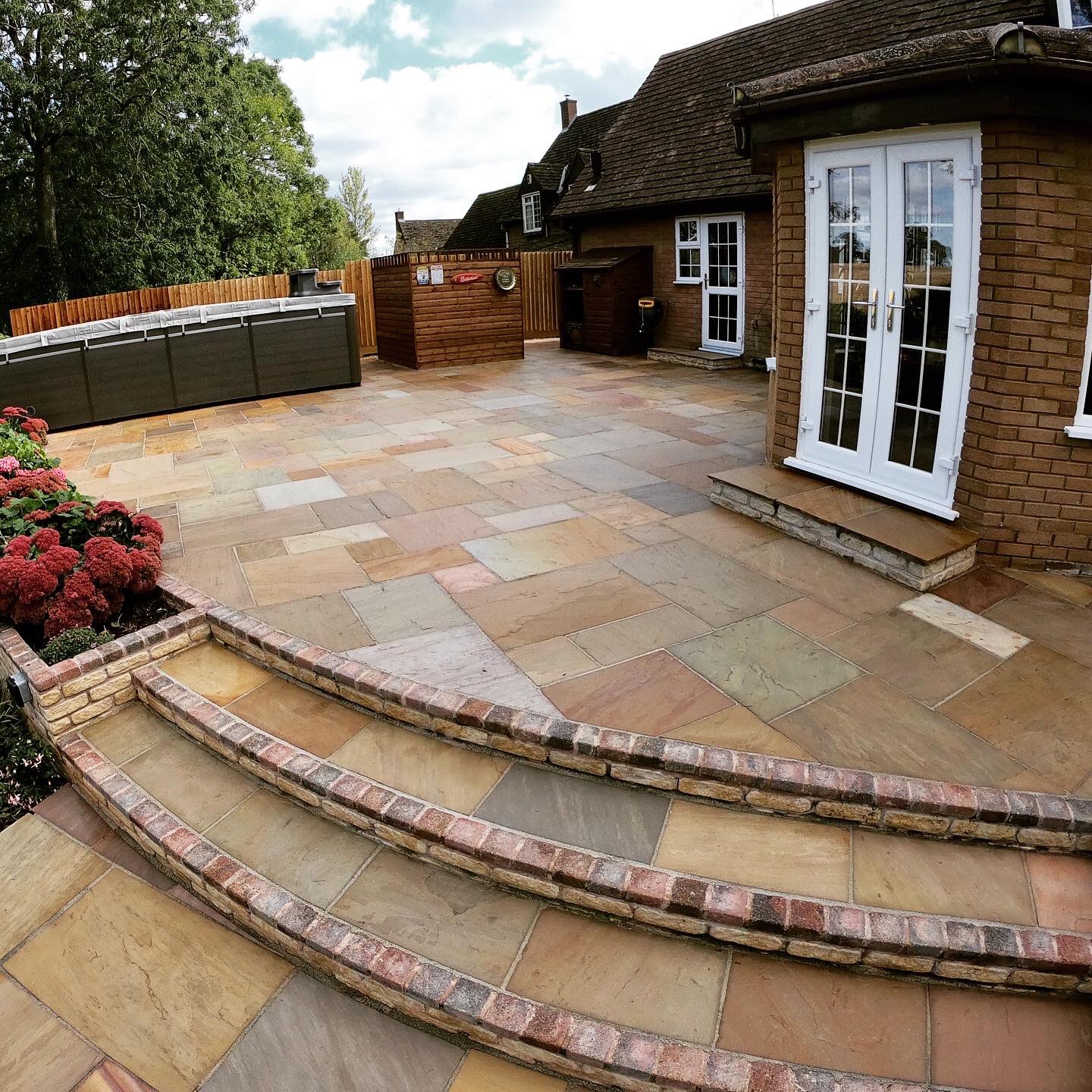 A well-maintained patio with natural stone paving, featuring steps and a garden area with flowers.