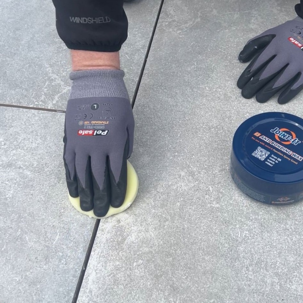 Person using a tool from the Joint It Porcelain Epoxy Grout Finishing and Smoothing Tool Set on grey tiles.