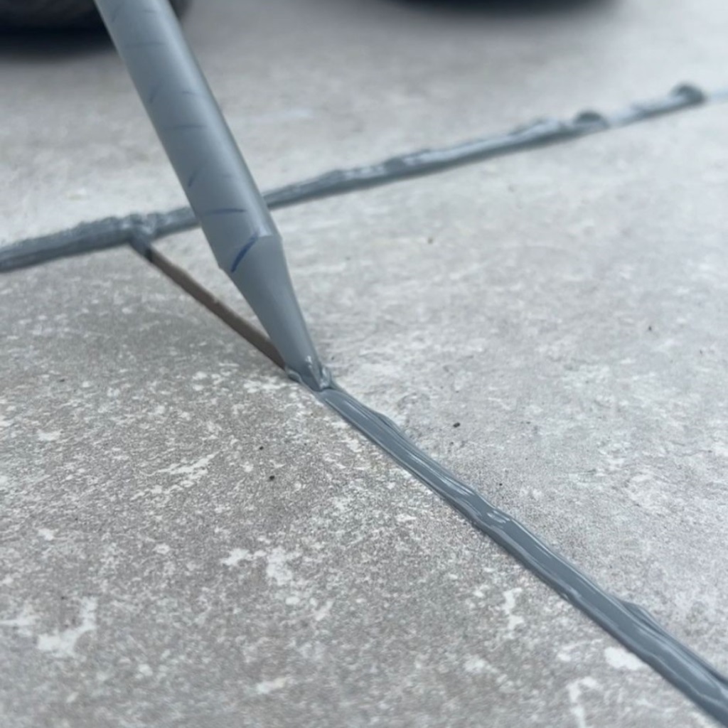 Close-up of a scraper removing grout from between porcelain tiles.
