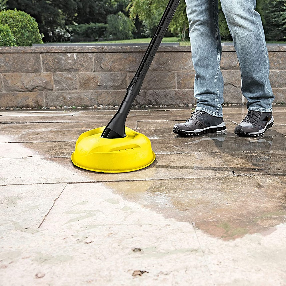 Person using a yellow patio cleaner attachment on a pressure washer to clean outdoor tiles.