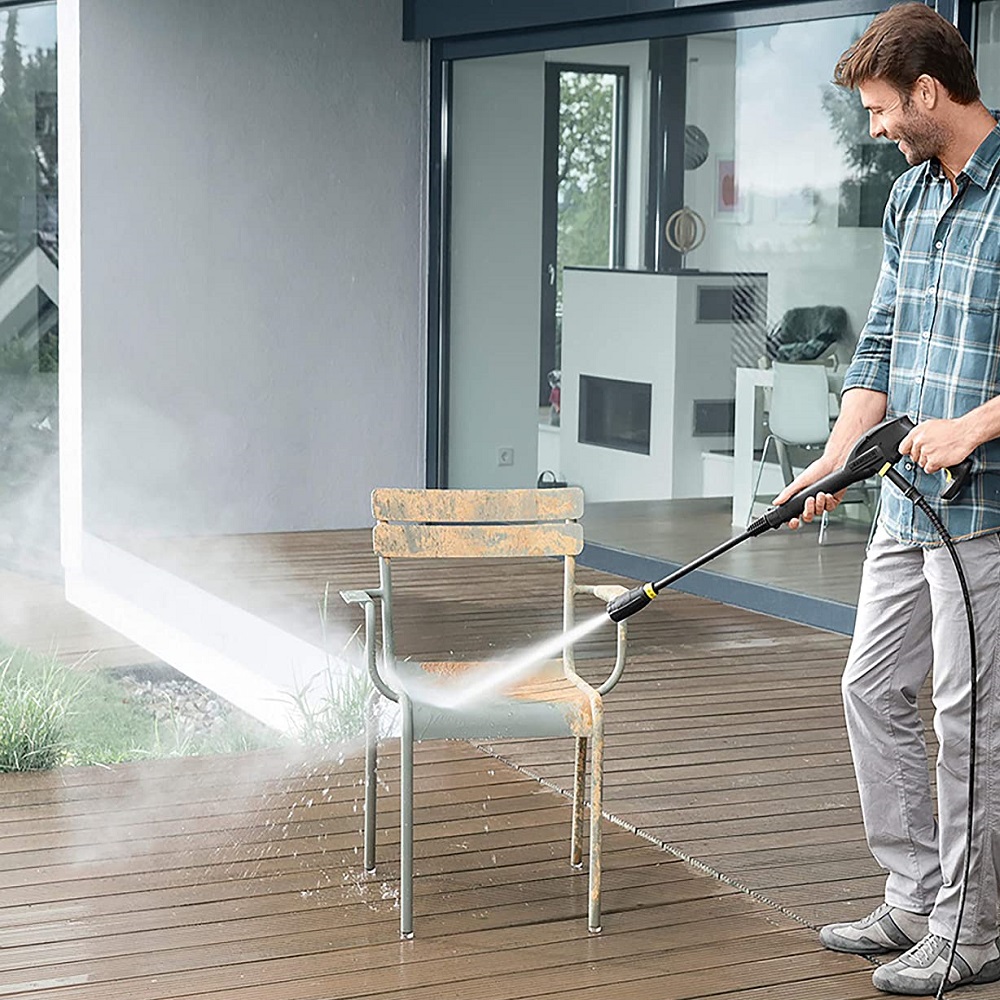 Person using a Karcher pressure washer to clean a wooden patio and metal chair.