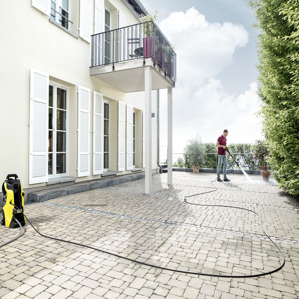 Person using a pressure washer with an extension hose on a patio.