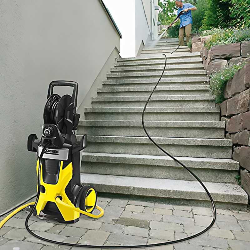 Person using a Karcher pressure washer with an extension hose on outdoor steps.