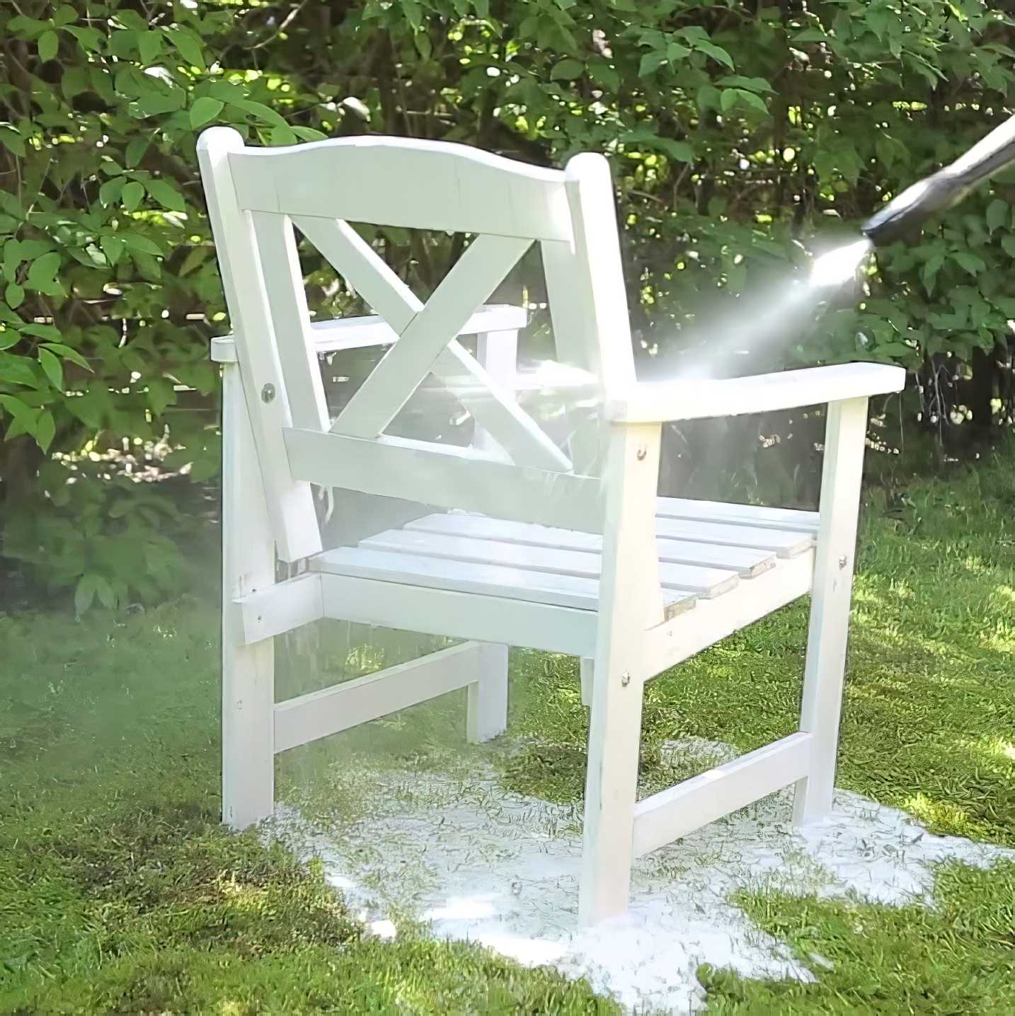 White wooden chair being cleaned with a pressure washer in a garden setting.