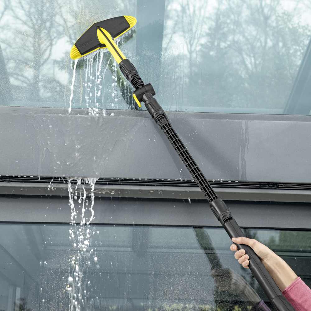 Person using a Karcher soft brush pressure washer to clean a glass surface.