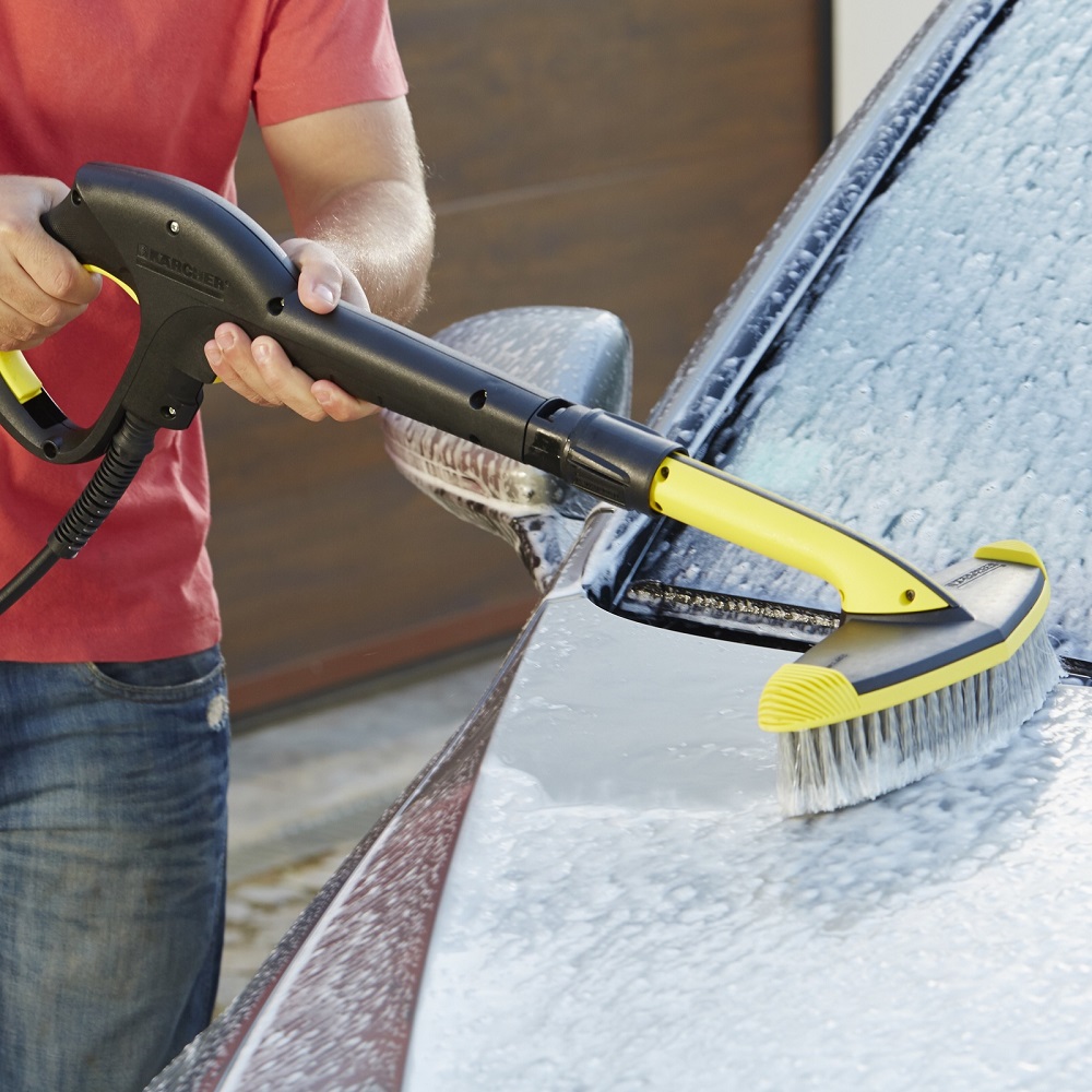 Person using a Karcher soft brush pressure washer to clean a car with soap suds.