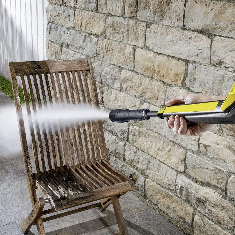 Person using a pressure washer to clean a wooden chair outdoors.