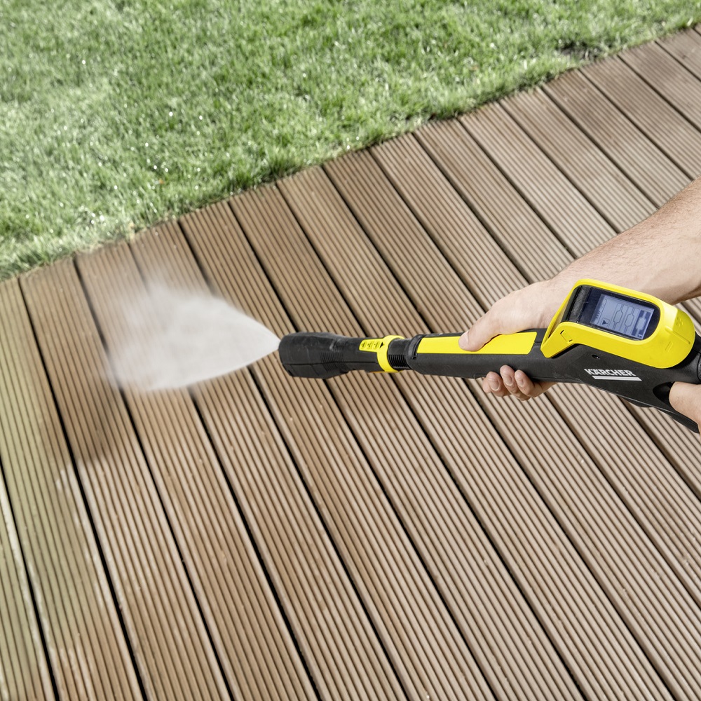 Person using a pressure washer on wooden decking.