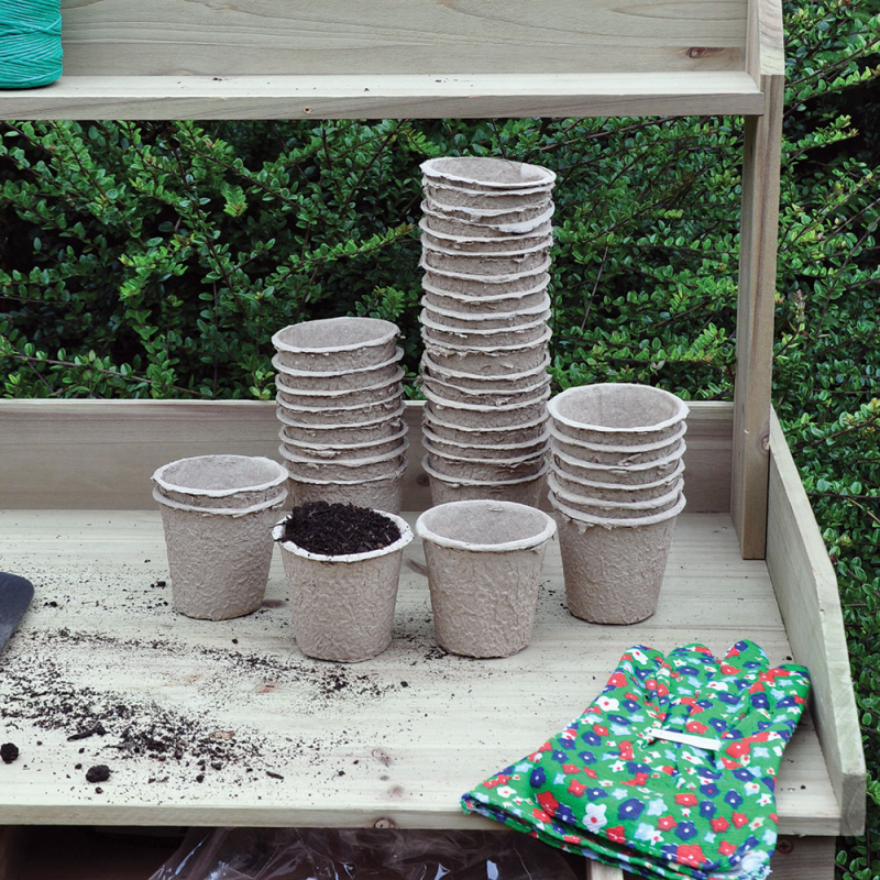 Biodegradable round peat pots stacked on a wooden surface with soil and gardening gloves nearby.