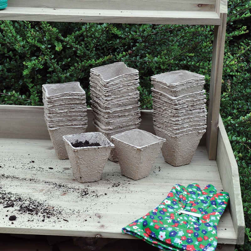 Stacks of biodegradable square peat pots on a wooden surface with gardening gloves nearby.