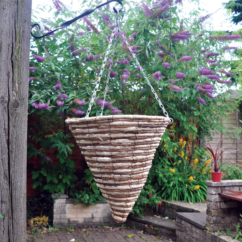 A 12-inch dark rattan willow wicker round hanging flower basket suspended in a garden setting with blooming flowers and greenery.