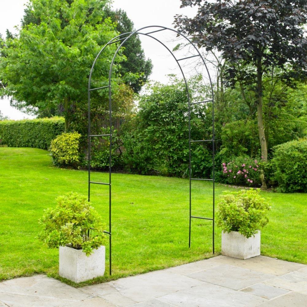 Metal archway for climbing plants in a garden setting with green grass and trees.