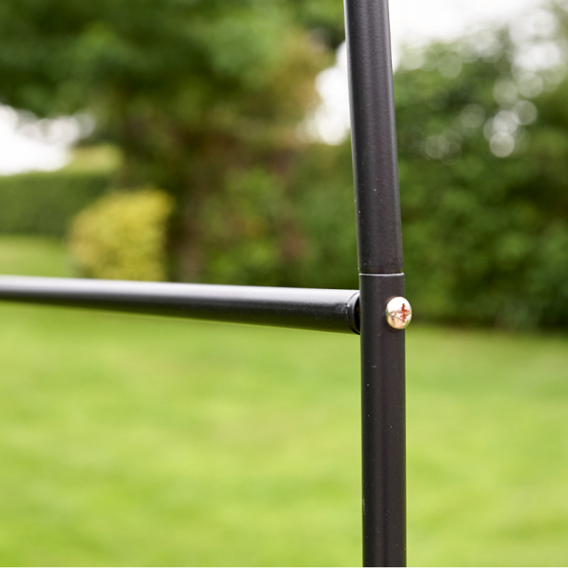 Close-up of a black tubular metal archway frame with a screw joint, set against a garden background.