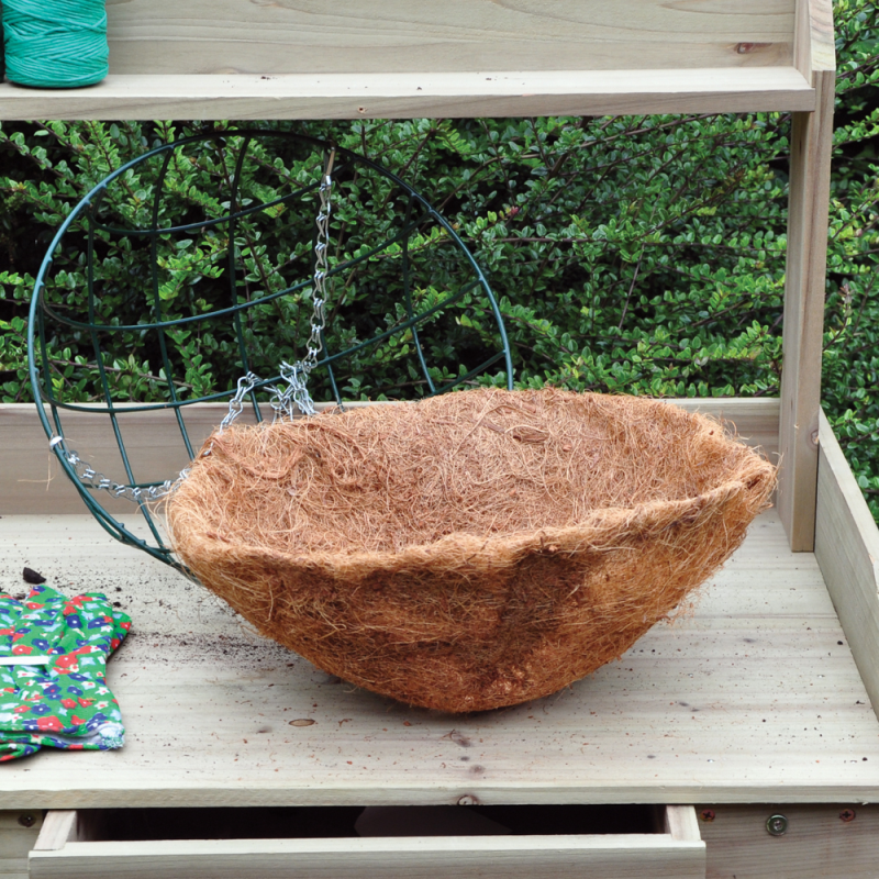 A 12 inch round hanging basket with a coco liner placed on a wooden surface, surrounded by gardening tools.