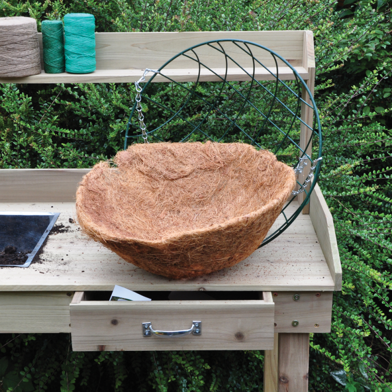 14 inch round flower hanging basket with coco liner on a wooden potting bench.