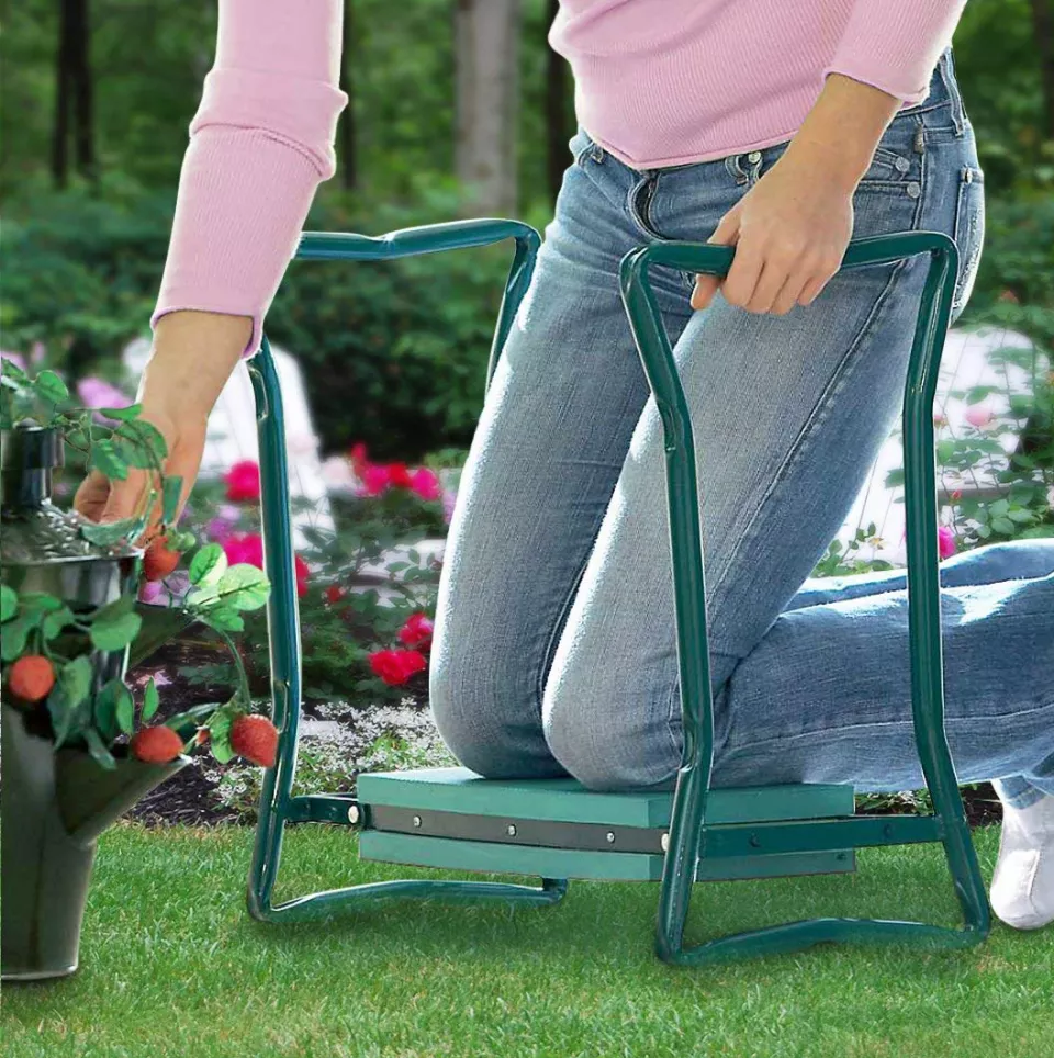 Person using a green garden kneeler with handles on grass, surrounded by flowers.