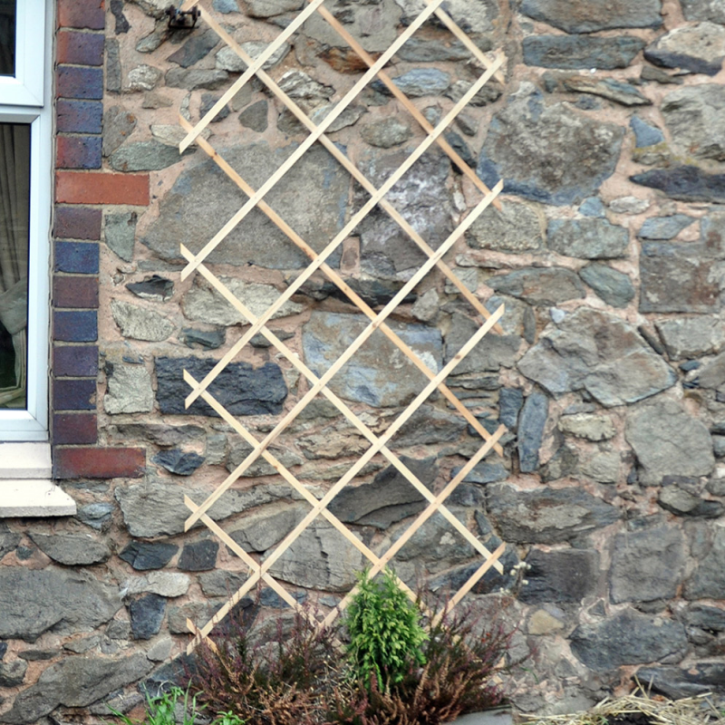 Wooden garden trellis attached to a stone wall, with plants growing at the base.
