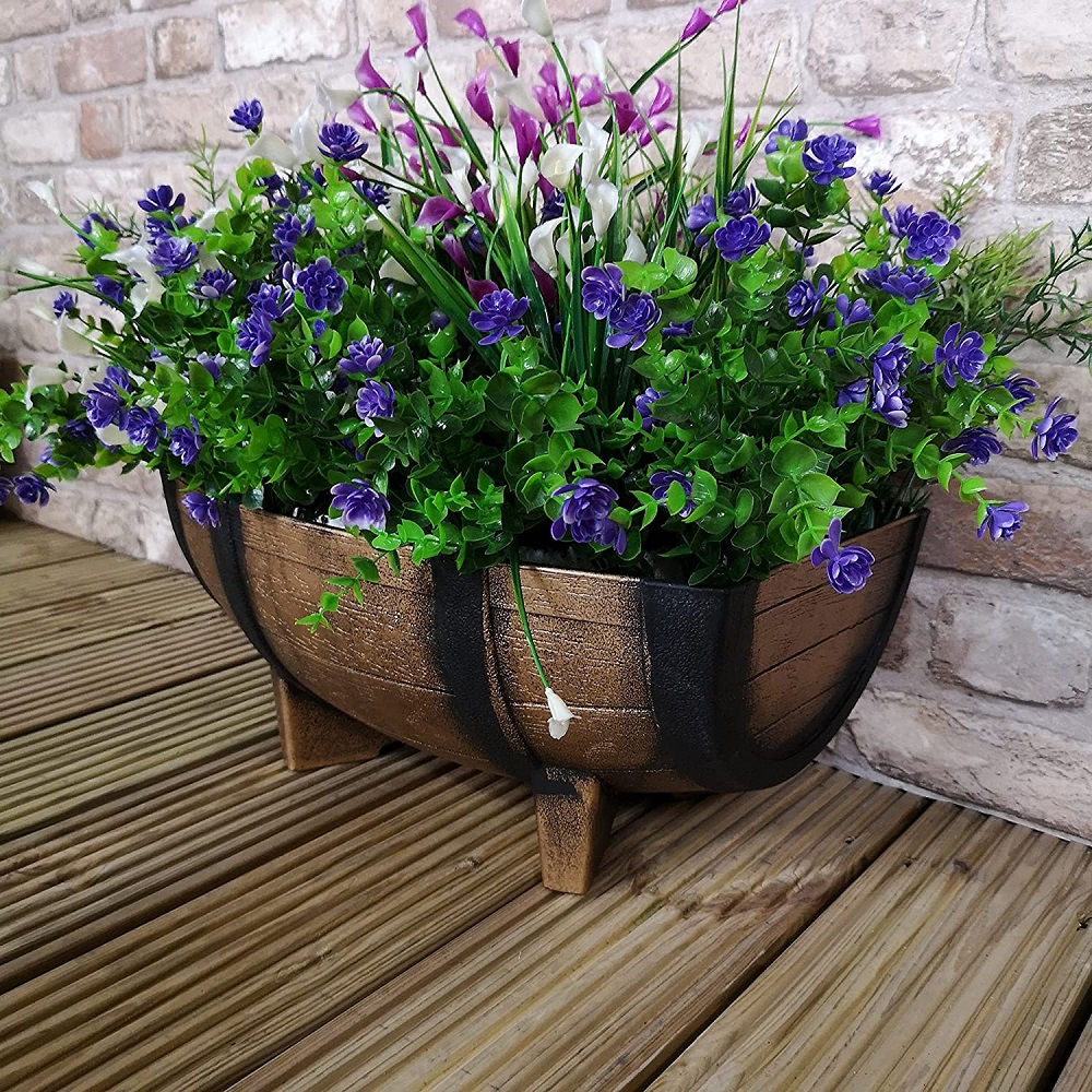 Wood effect half barrel plastic planter with purple and white flowers on a wooden deck.