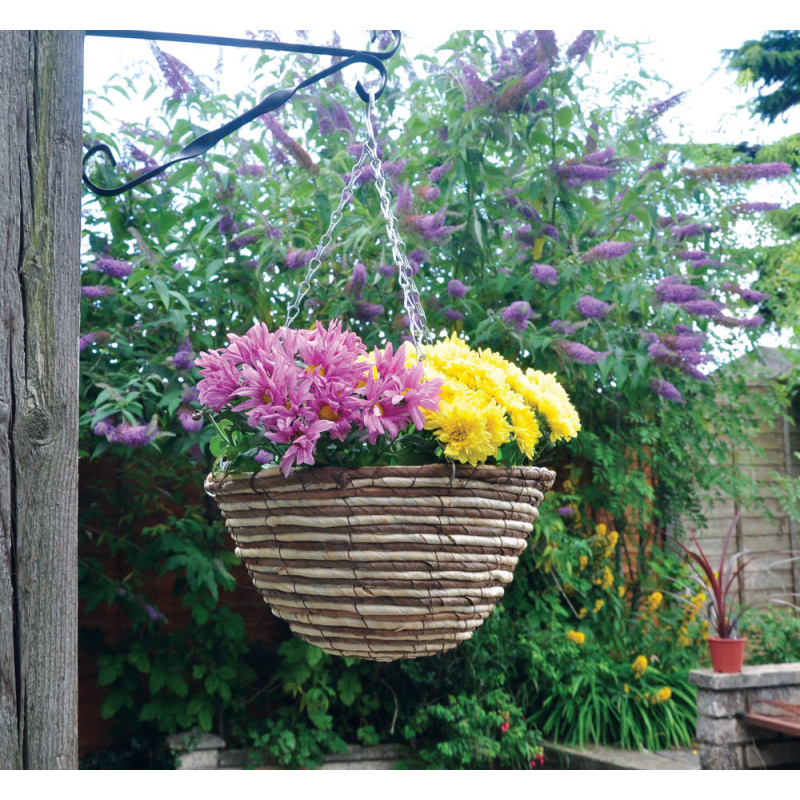Hanging flower basket with pink and yellow flowers in a garden setting.