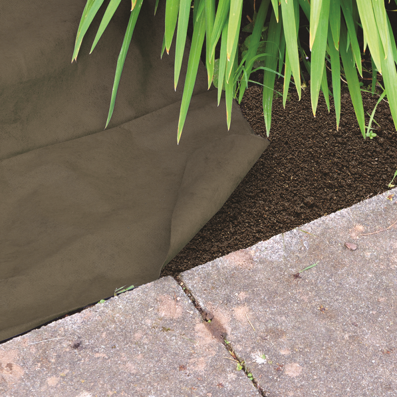 Garden weed control fabric laid on soil beside green plants and paving stones.