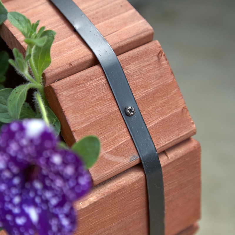 Close-up of a wooden planter with metal strap detail and a purple flower.