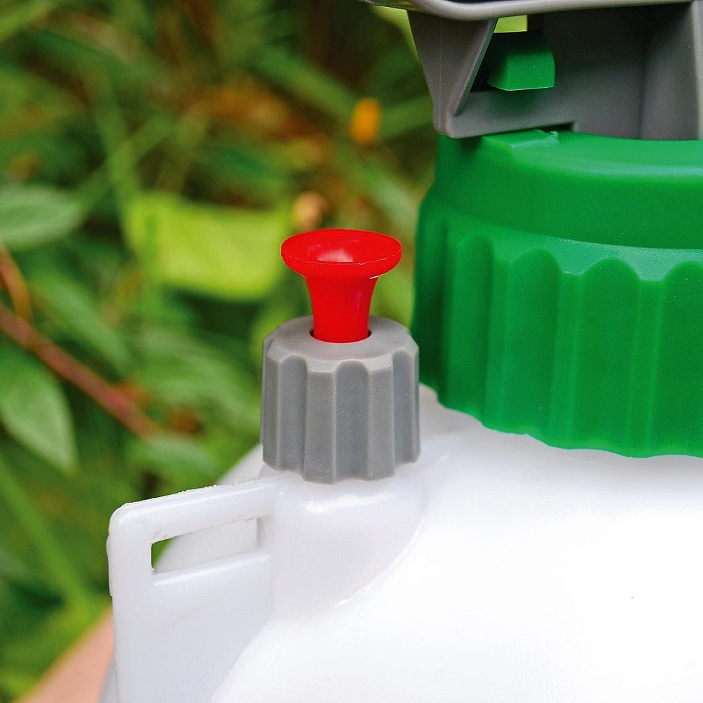 Close-up of a garden hand pump pressure sprayer with a red and grey nozzle, green cap, and white body.