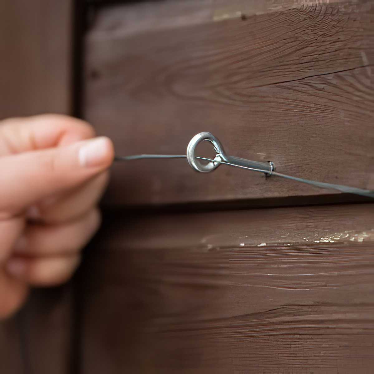A person securing galvanised garden wire to a wooden structure.