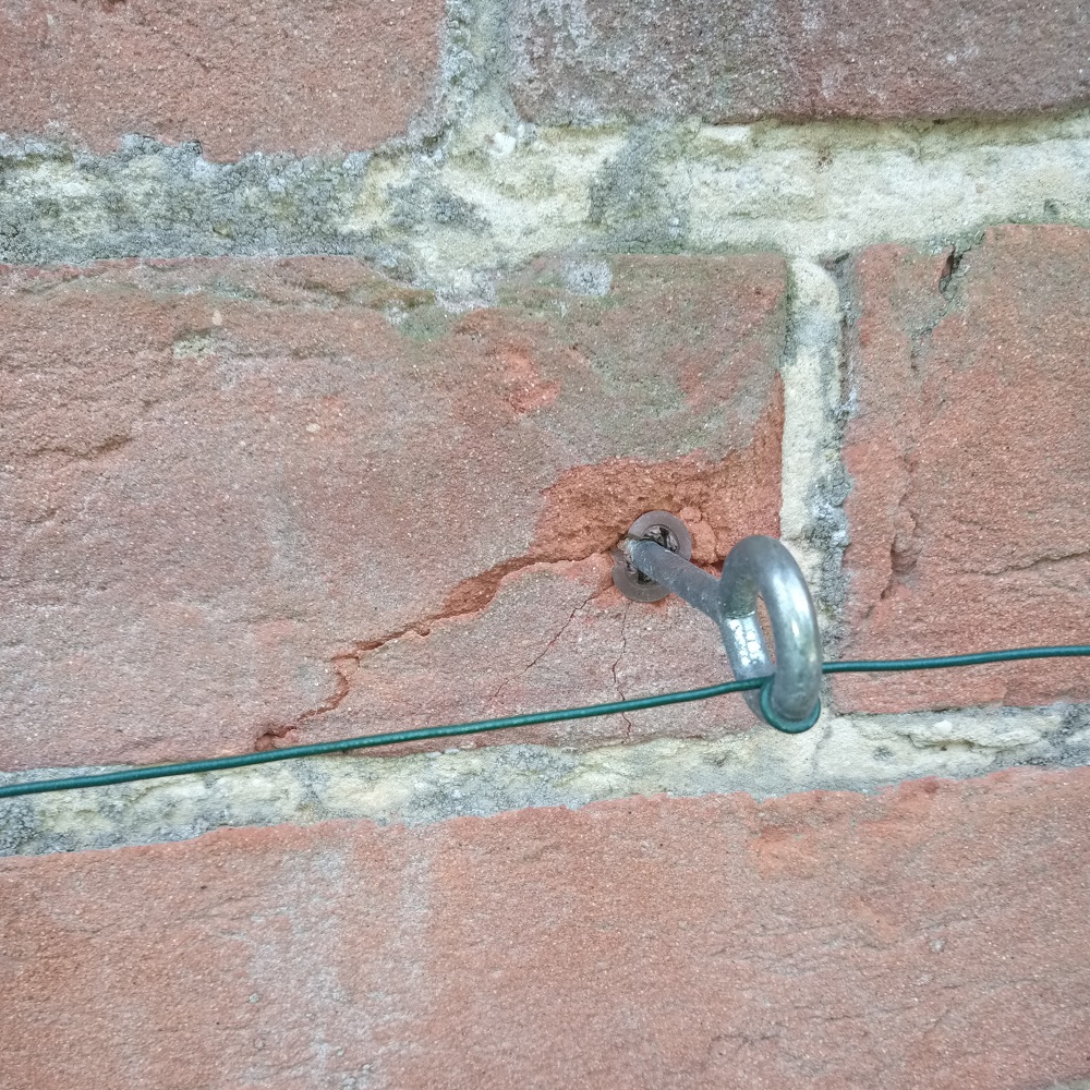 Galvanised garden wire attached to a brick wall using a metal hook.