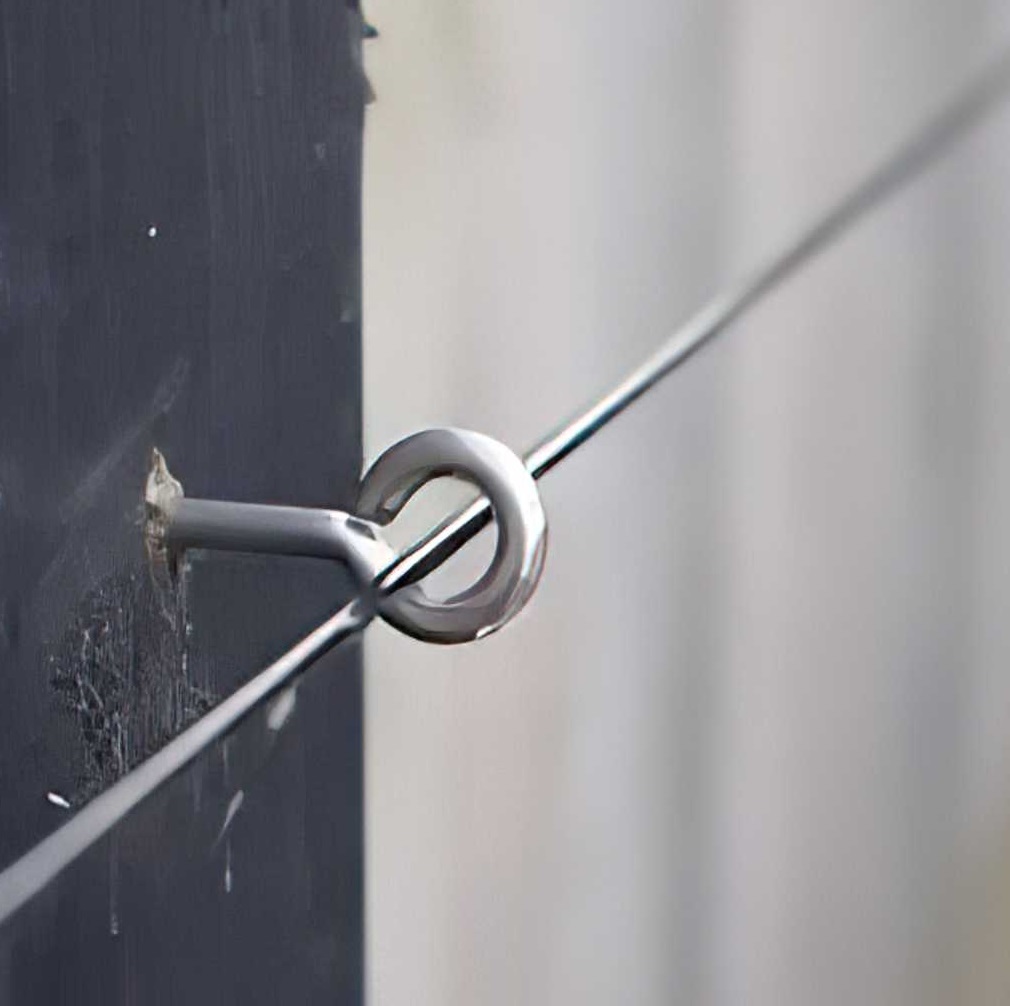 Close-up of galvanised garden wire threaded through a metal eyelet on a wooden surface.