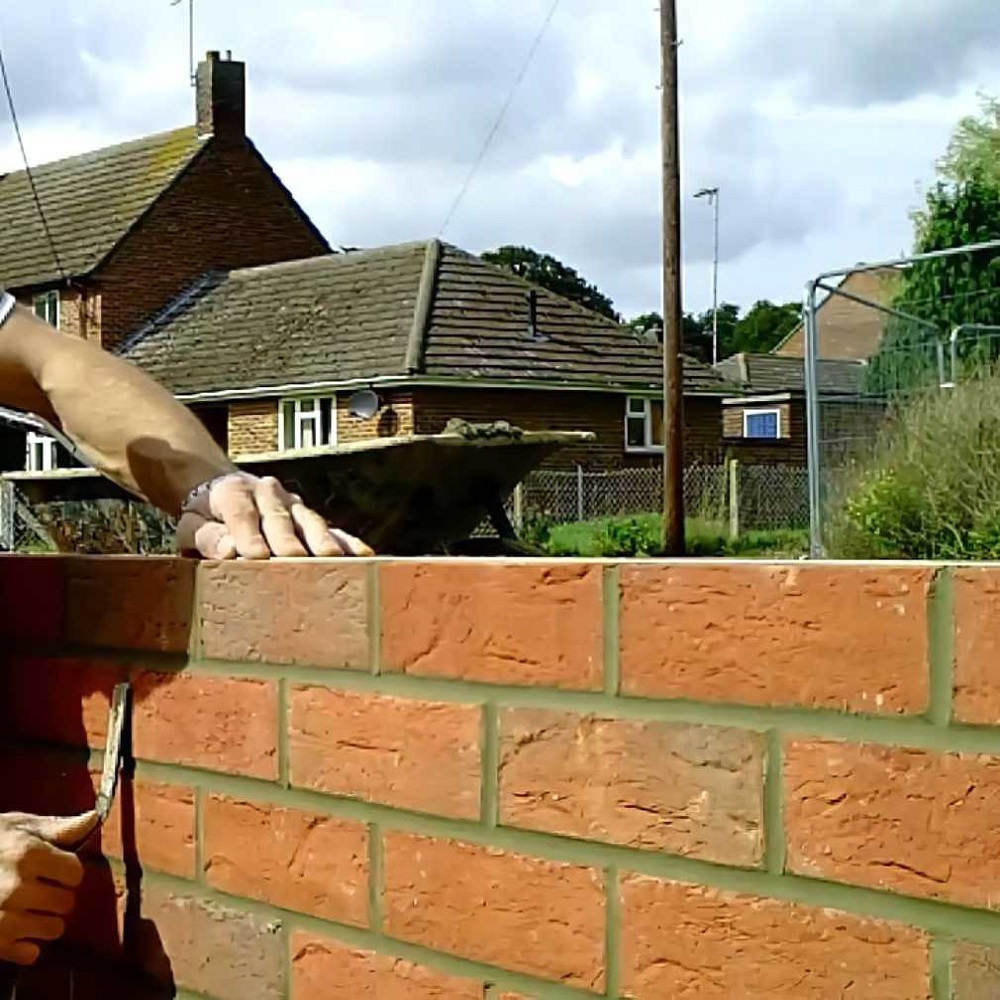 Person using a brick mortar jointer on a newly built brick wall.