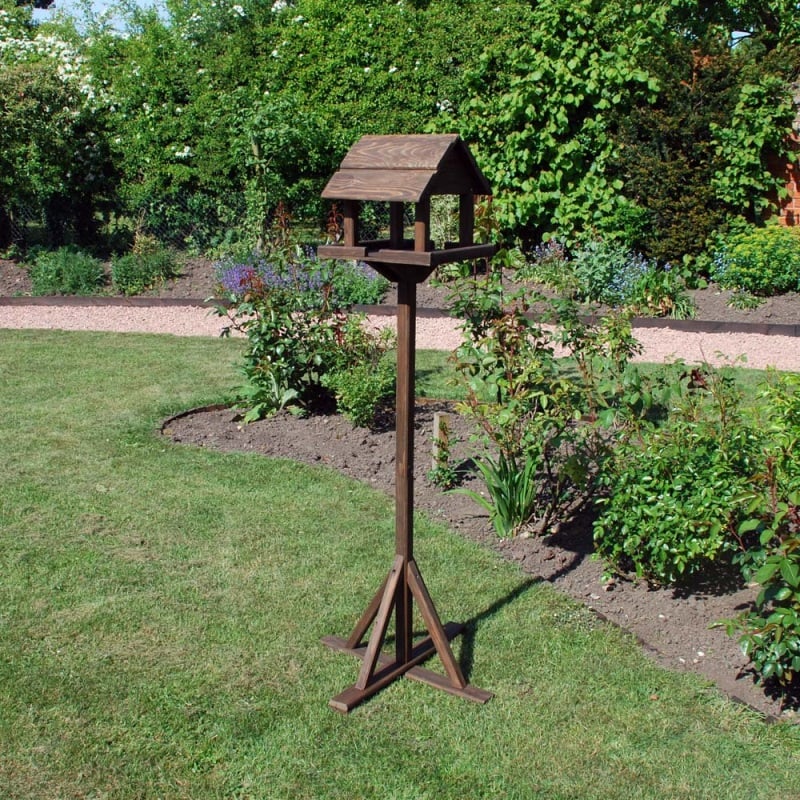 Wooden bird table in a garden setting with green foliage and a pathway.