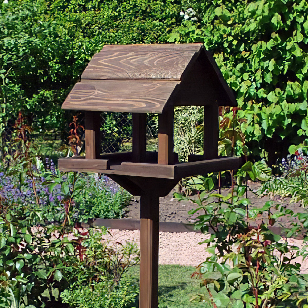 Rustic wooden bird table in a garden setting with greenery and flowers.
