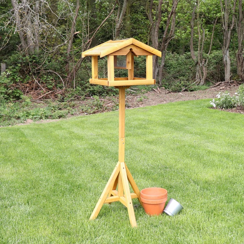 Wooden bird table with built-in nut feeder standing on a grassy lawn.