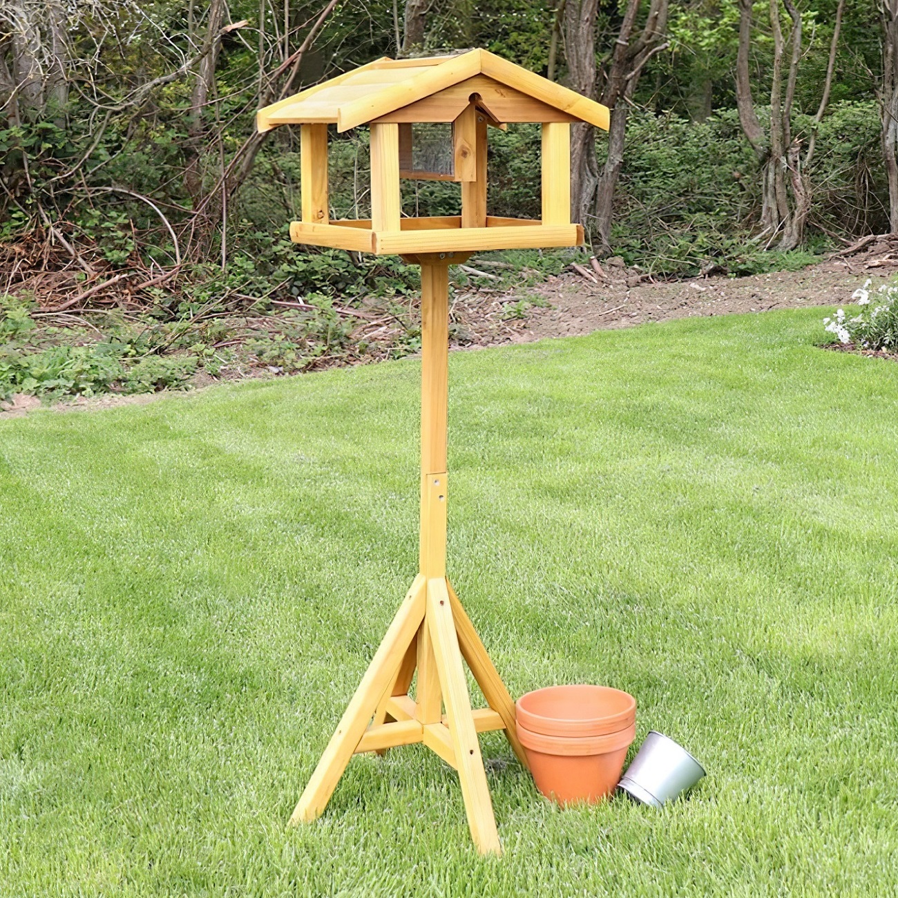 Wooden bird table with built-in nut feeder standing on a grassy lawn.