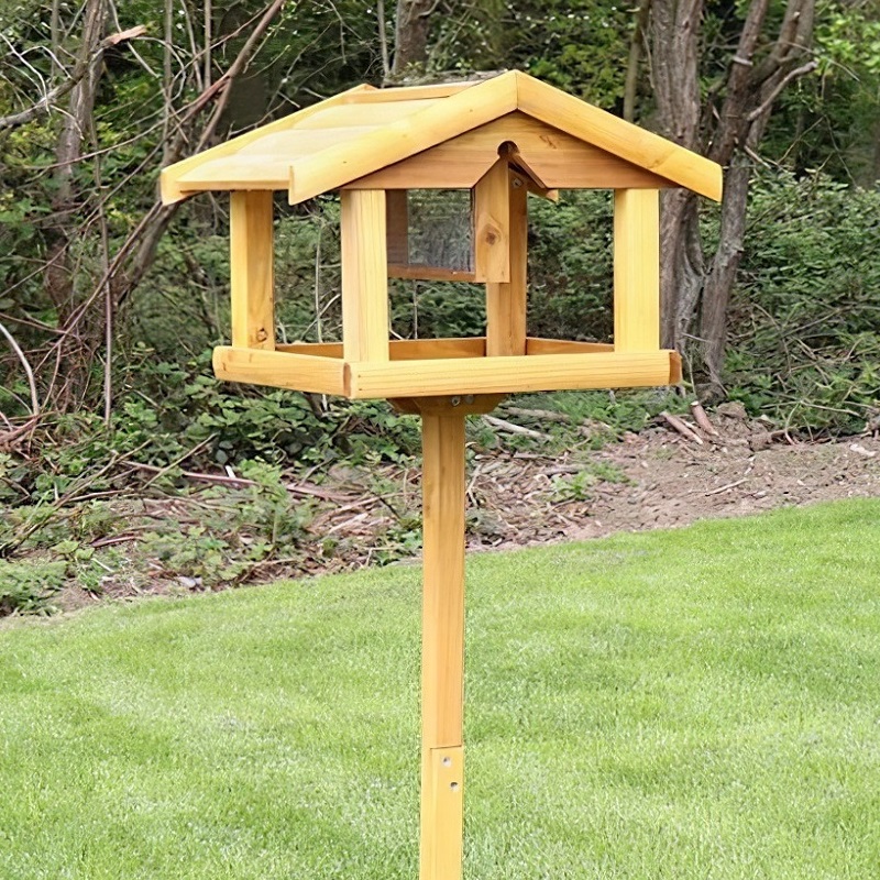 Wooden bird table with built-in nut feeder on a grassy lawn, surrounded by trees.
