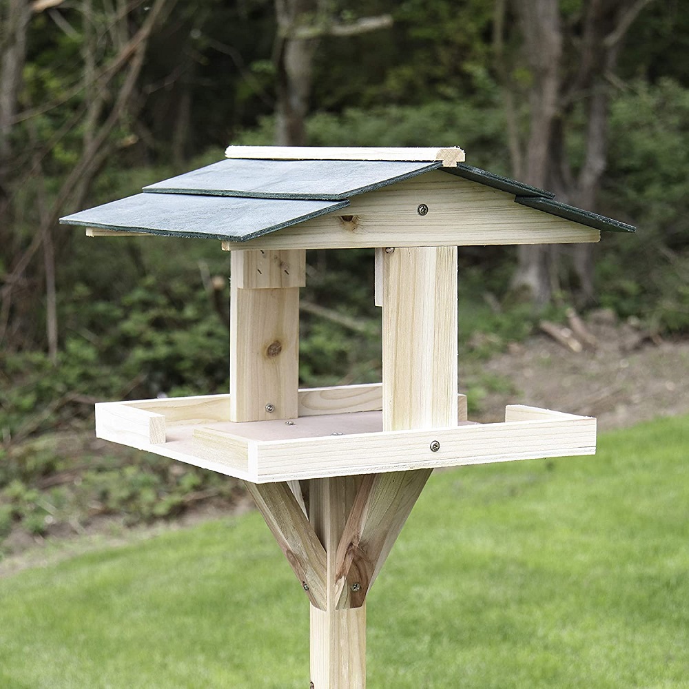 Wooden garden bird table with a green roof set in an outdoor environment.
