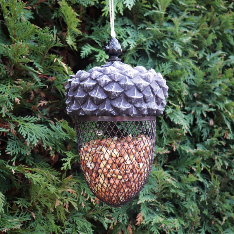 Hanging acorn-shaped bird feeder filled with seeds against a backdrop of green foliage.