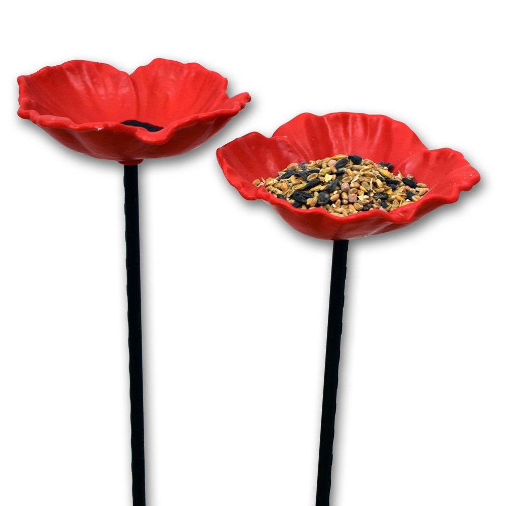Red poppy-shaped bird feeders on black stems, one filled with mixed bird seed.