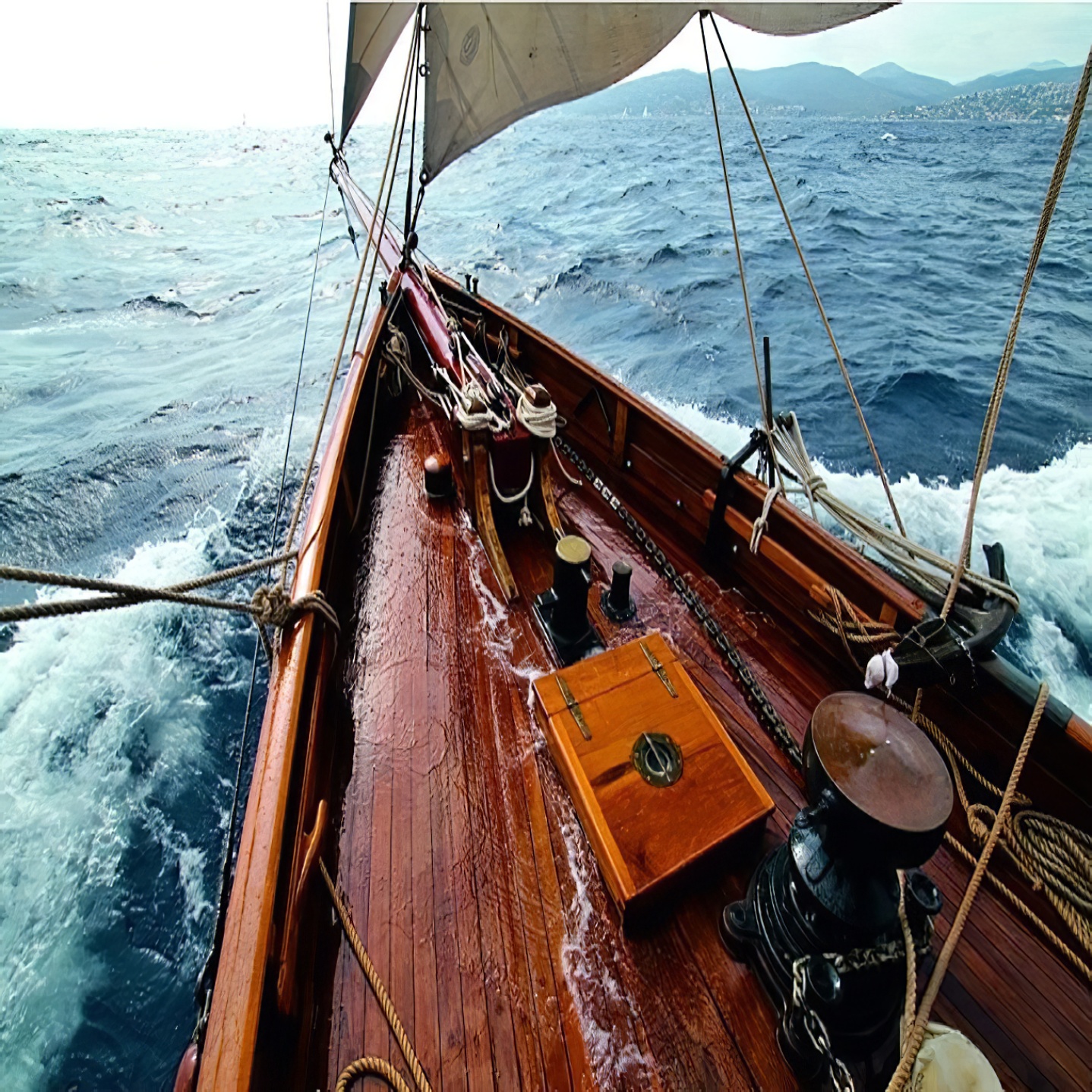 Wooden deck of a yacht sailing on the ocean with visible ropes and equipment.