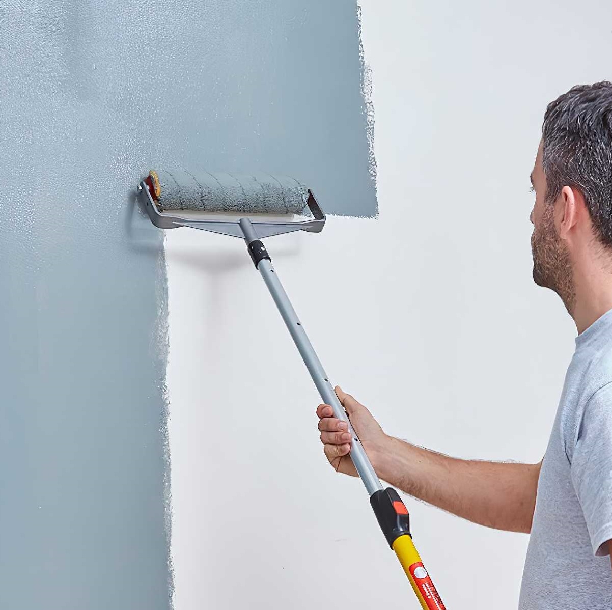 Person using a Prodec 12 Inch Solvent Resistant Industrial Paint Roller Sleeve to apply grey paint on a wall.