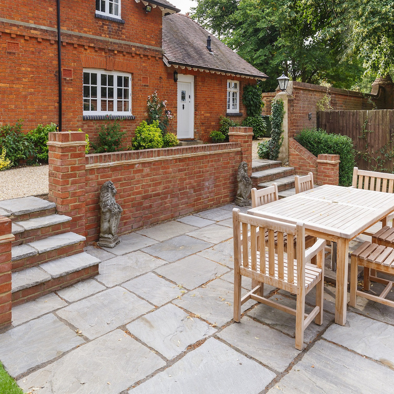Patio with Indian sandstone paving and wooden outdoor furniture set in a garden.