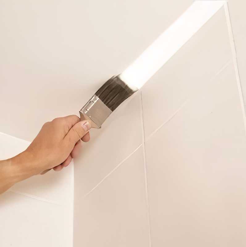 Hand applying white paint with a brush on a wall corner.