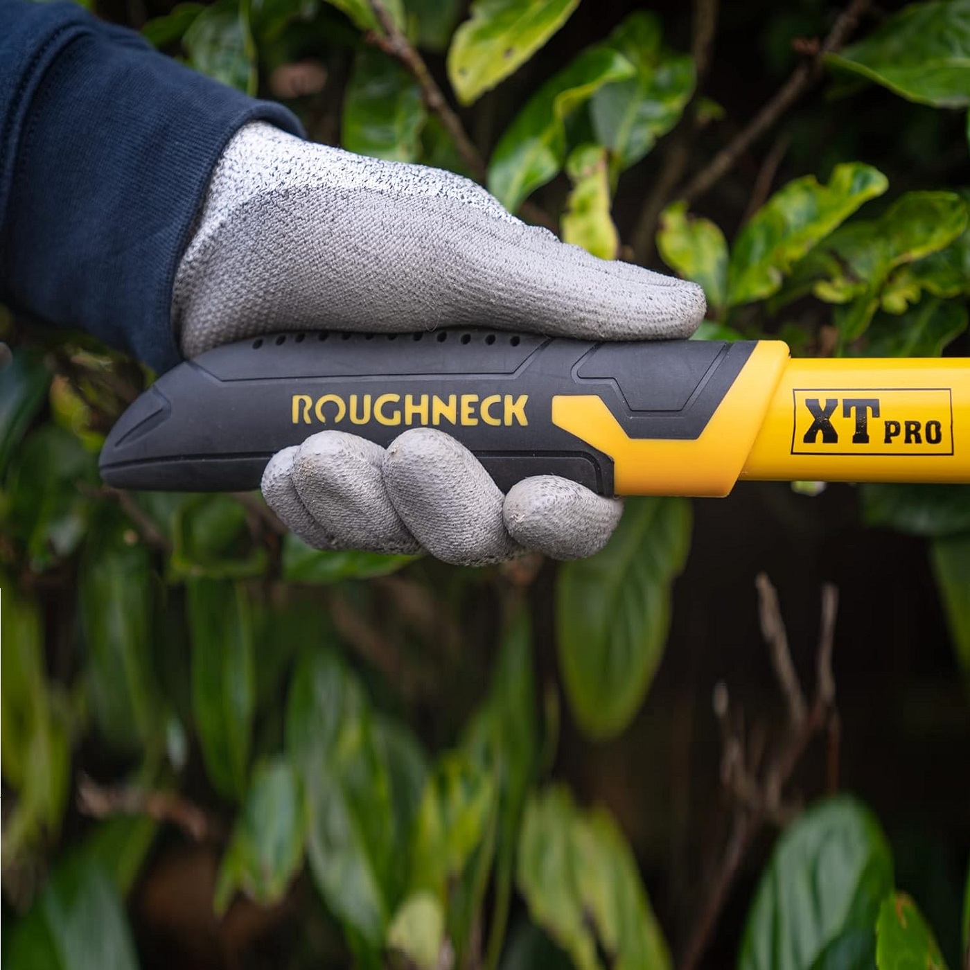 Gloved hand holding Roughneck XT PRO Heavy Duty Garden Bypass Lopping Shears with foliage in the background.