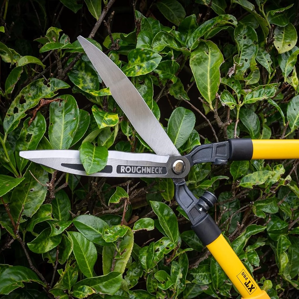 Roughneck XT PRO hedge and grass shears with wavy blades cutting through green foliage.