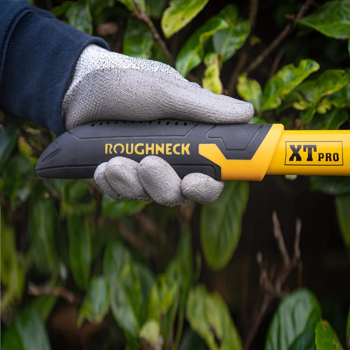 Close-up of a gloved hand holding the handle of Roughneck XT PRO Heavy Duty Wavy Blade Hedge and Grass Shears.