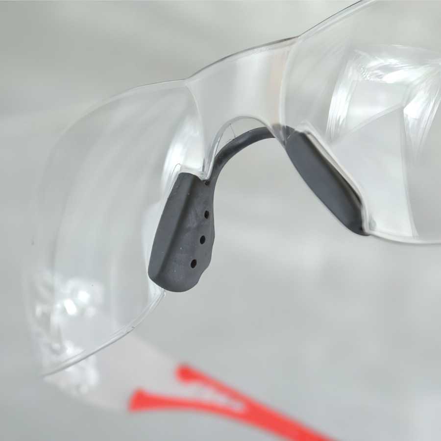 Close-up of clear safety glasses with black nose pad and red temple tips.