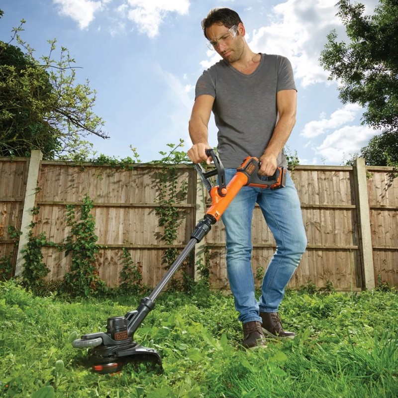 Person wearing clear safety glasses while using a garden trimmer in a grassy area.