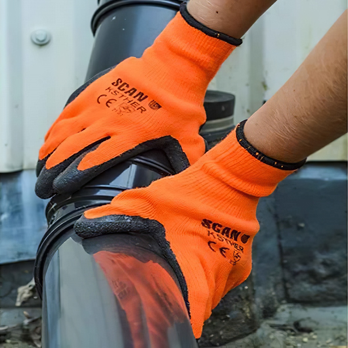 Person wearing orange hi-vis latex thermal work gloves handling a pipe.