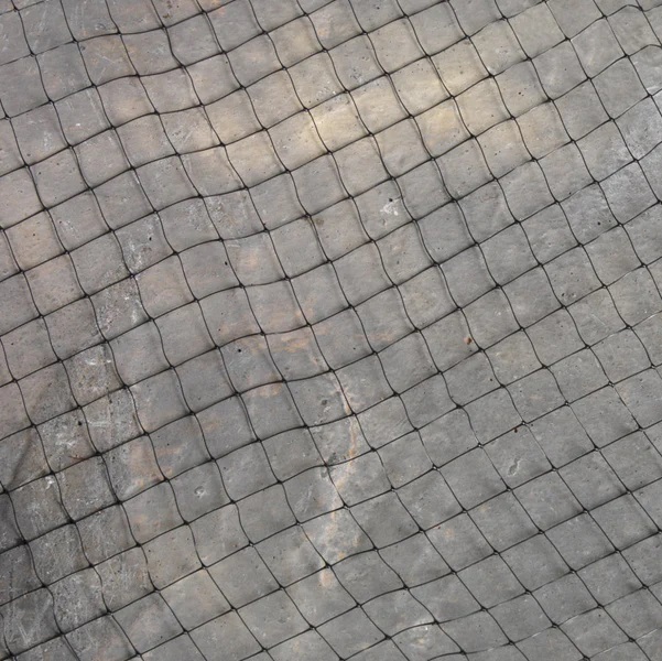 Close-up view of black garden netting laid on a concrete surface.